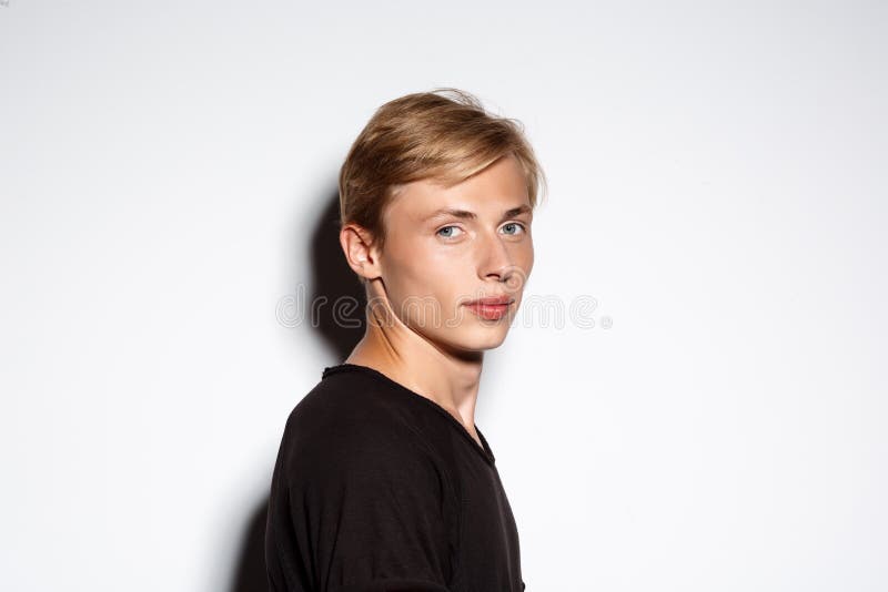Sluit portret van de zekere blonde knappe jonge mens die zwarte die t-shirt dragen op witte achtergrond omhoog wordt geïsoleerd stock afbeelding Sluit portret van de zekere blonde knappe jonge mens die zwarte die t-shirt dragen op witte achtergrond omhoog wordt geïsoleerd stock afbeelding