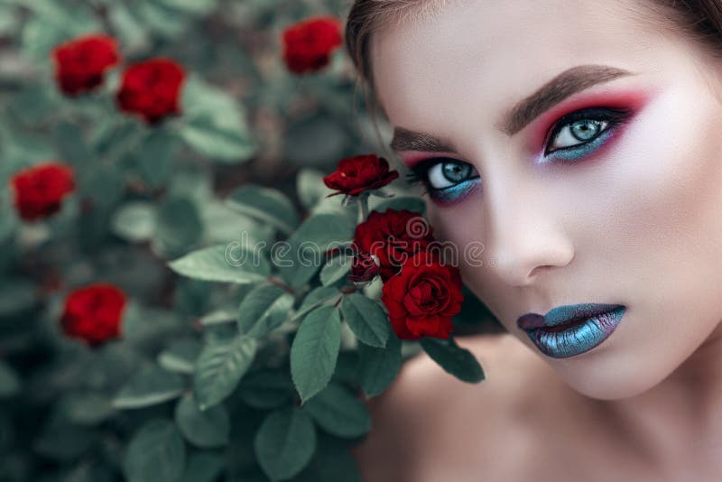 Sluit portret van jong mooi model met artistiek maken omhoog omhoog het zitten in de rode roze struik en het kijken recht royalty-vrije stock afbeeldingen Sluit portret van jong mooi model met artistiek maken omhoog omhoog het zitten in de rode roze struik en het kijken recht royalty-vrije stock afbeeldingen
