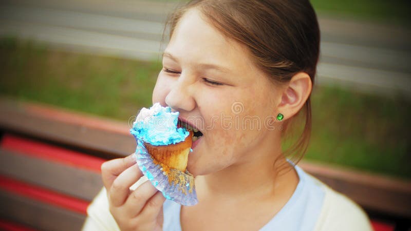 Sluit van aanbiddelijk omhoog weinig vet meisje die een cake met haar handen eten zittend op een bank in het park