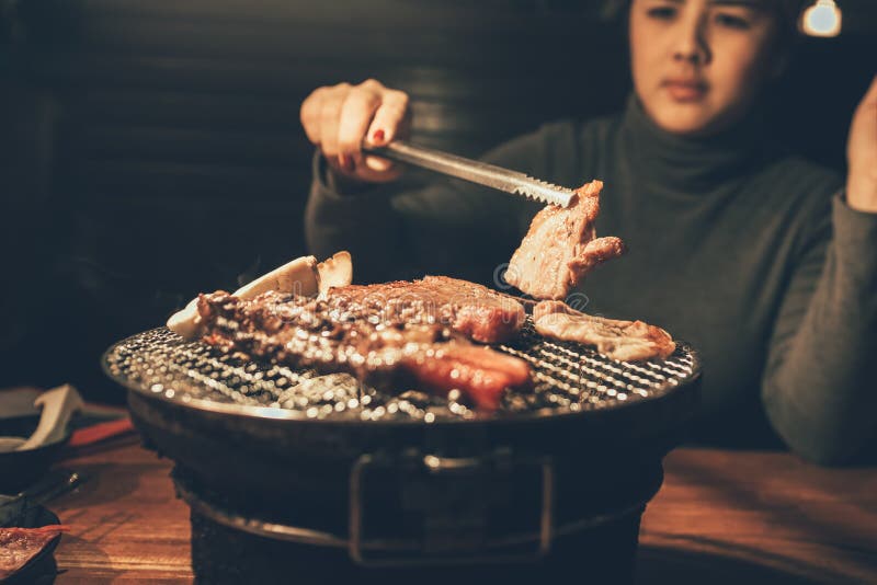 Sluit vlees van het vrouwen omhoog het kokende varkensvlees op een houtskoolgrill in restaura royalty-vrije stock afbeeldingen Sluit vlees van het vrouwen omhoog het kokende varkensvlees op een houtskoolgrill in restaura royalty-vrije stock afbeeldingen
