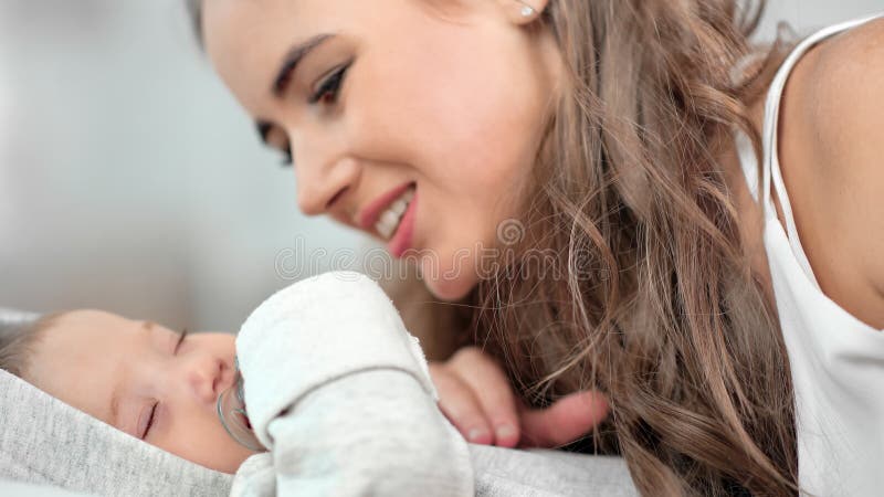 Sluiten van een gelukkig moeder die haar kleine slapende baby's vreugde en positieve emotie heeft gekust