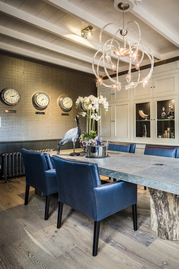 This office space can also be used as a dining area. The stone table top and petrified wood legs give the table a modern feel. Blue,faux leather chairs complement the bouquets on the table and the taxidermist crane bird. The modern chandelier hangs from a white ceiling and adds extra flair. This office space can also be used as a dining area. The stone table top and petrified wood legs give the table a modern feel. Blue,faux leather chairs complement the bouquets on the table and the taxidermist crane bird. The modern chandelier hangs from a white ceiling and adds extra flair.