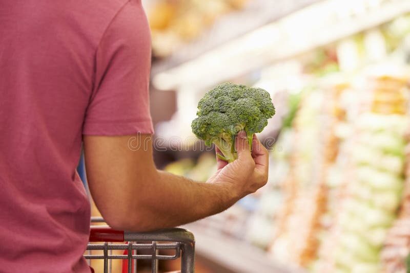 Slut upp av mannen som väljer broccoli i supermarket arkivbilder Slut upp av mannen som väljer broccoli i supermarket arkivbilder