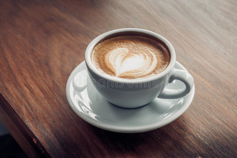 Slut upp den varma cappuccinokaffekoppen med konst för hjärtaformlatte på royaltyfri bild Slut upp den varma cappuccinokaffekoppen med konst för hjärtaformlatte på royaltyfri bild