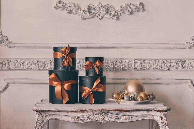 Wrapped gift black boxes with ribbons as Christmas presents on a table on luxury white wall design bas-relief stucco mouldings roccoco elements. Wrapped gift black boxes with ribbons as Christmas presents on a table on luxury white wall design bas-relief stucco mouldings roccoco elements.