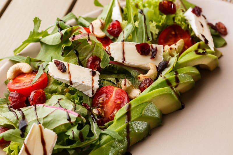 Smaklig och sund sallad med arugula, brien, ost, avokadot, körsbärsröda tomater, den torra tranbäret och kasjuer Top besk?dar _ royaltyfri foto Smaklig och sund sallad med arugula, brien, ost, avokadot, körsbärsröda tomater, den torra tranbäret och kasjuer Top besk?dar _ royaltyfri foto