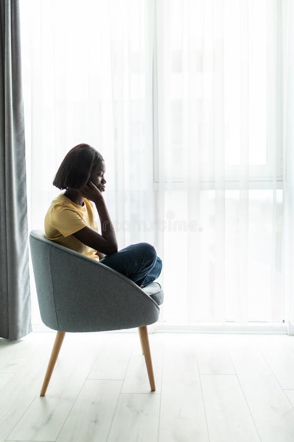 Smaklig, stressad afrikansk flicka som sitter i stolen och sitter hemma och tillbringar helgen ensam royaltyfri foto