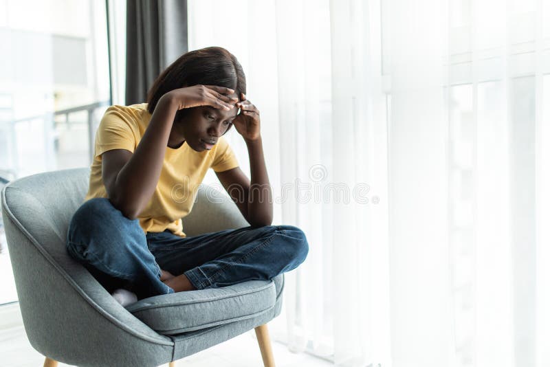 Smaklig, stressad afrikansk flicka som sitter i stolen och sitter hemma och tillbringar helgen ensam arkivfoton