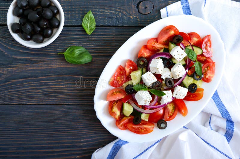 Smaklig vitaminsallad med nya grönsaker, feta, svarta oliv, basilikasås på en vit platta på en träbakgrund Top besk?dar royaltyfria bilder Smaklig vitaminsallad med nya grönsaker, feta, svarta oliv, basilikasås på en vit platta på en träbakgrund Top besk?dar royaltyfria bilder
