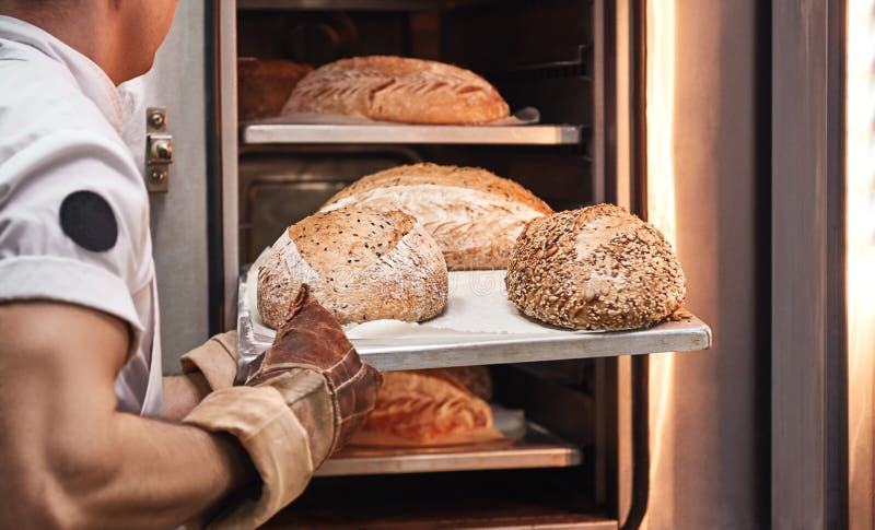 Smakligt och nytt Bagares händer i arbetande handskar som ut tar nytt bakat bröd från ugnen på köket royaltyfria foton Smakligt och nytt Bagares händer i arbetande handskar som ut tar nytt bakat bröd från ugnen på köket royaltyfria foton