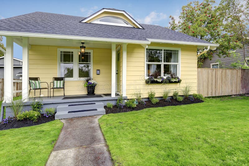 Small American yellow house exterior. Covered porch with stairs and well kept lawn in the front yard. Northwest, USA