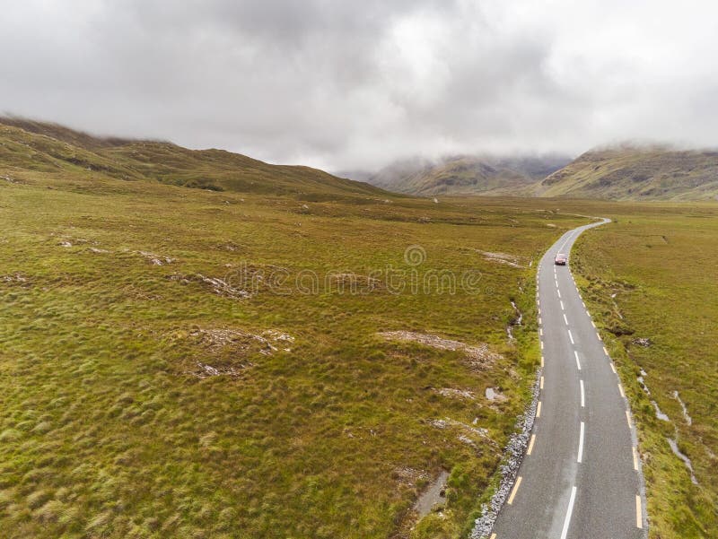 Small asphalt road into mountains. Aerial drone view, Connemara region, West of Ireland. Cloudy sky. Empty wild fields on each