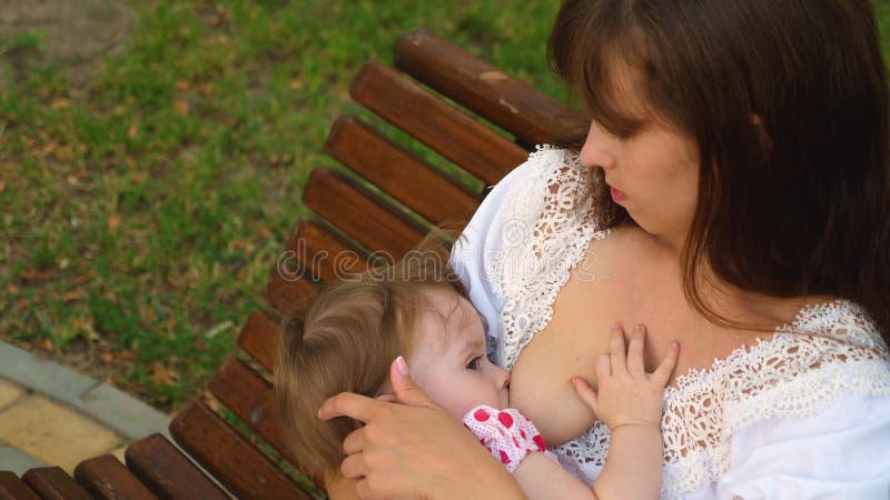 Small Baby Sucks Milk from His Mom Breast. Mom is Breastfeeding Child Sitting on Park Bench Stock Footage - Video of street, feeding: 121430836