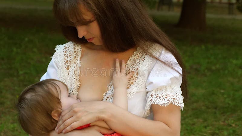 Small Baby Sucks Milk from His Mom Breast. Mom is Breastfeeding Child Sitting on Park Bench and Smiling Stock Video - Video of recreation, motherhood: 120777937