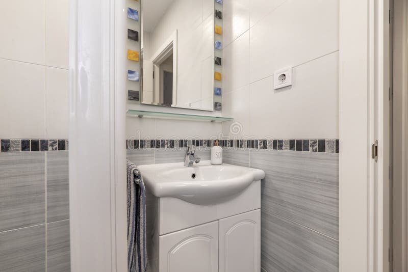 Small bathroom with white wooden furniture, porcelain sink, mirror cabinet, mirror with colored frame, white shower cabin with