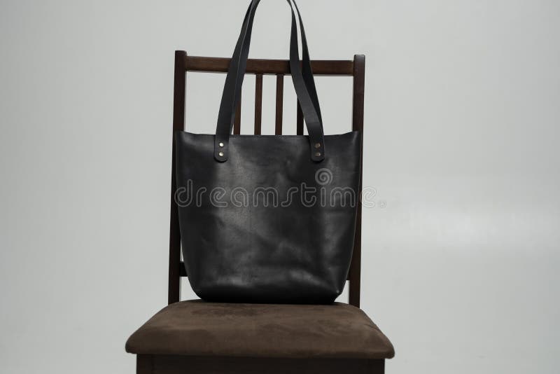 Small black leather bag on a brown wooden chair with a white background. Shoulder handbag. Style, retro, fashion