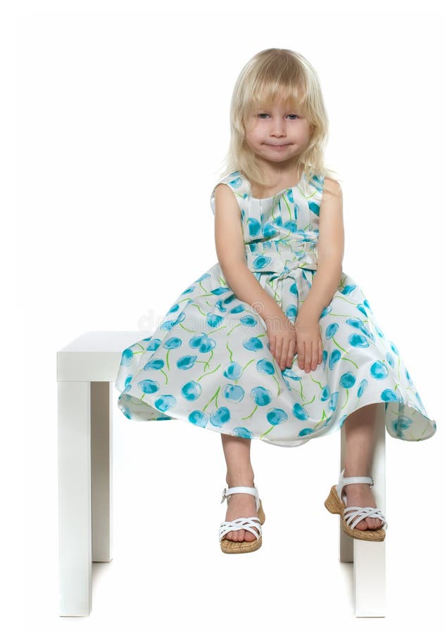 Small blond girl in white-blue dress sits on white chair, isolated on white. Small blond girl in white-blue dress sits on white chair, isolated on white