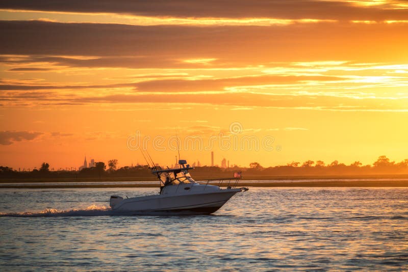 Small boat sailing through water as the sun sets. Skyline seen in the background.