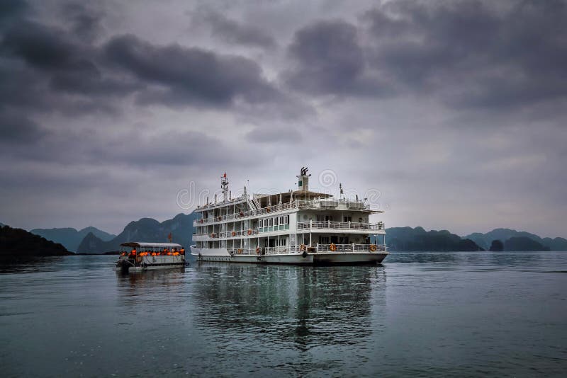 A small boat with tourist arrives at the large cruise ship that is anchored in Ha Long bay