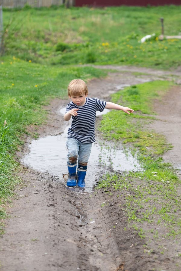 A Small Boy in Rubber Boots Walks through a Muddy Puddle Stock Image