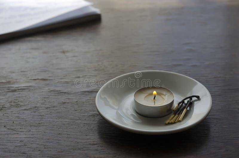 A Small Burning Candle and a Group of Burnt Matches in a Saucer on the