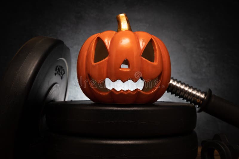 Halloween pumpkin decoration on heavy gym dumbbell barbell weights.