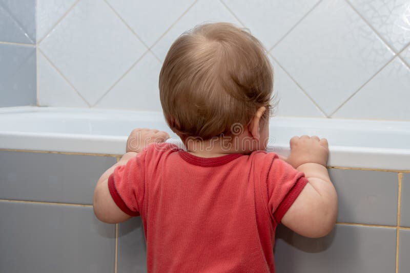 A small child in the bathroom looking into the bath, holding the edge stock photography
