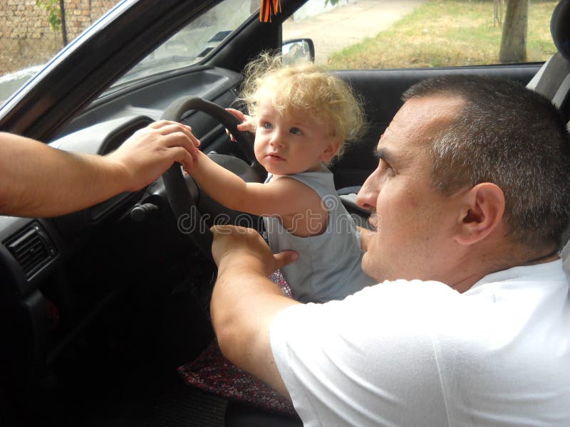 A small child is driving a car. A middle-aged father supports him with his hands. The boy plays in the driver of the car royalty free stock images A small child is driving a car. A middle-aged father supports him with his hands. The boy plays in the driver of the car royalty free stock images