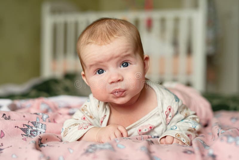 Small child lies on his stomach, drooling with bubbles on  lips, girl holds her head with difficulty,