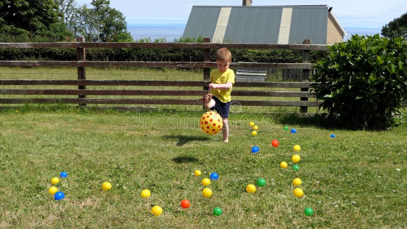 Small Child playing with balls and toys on a lawn in a garden on sunny day