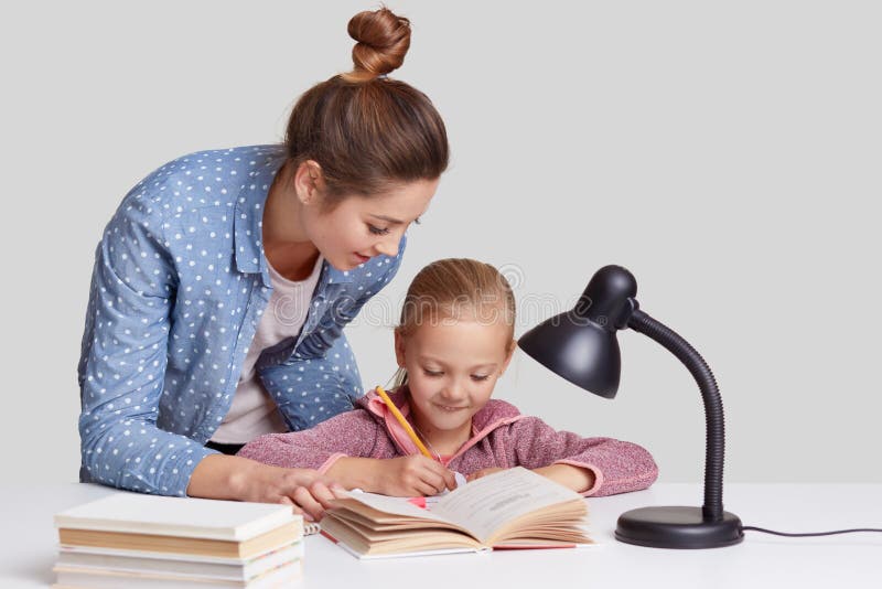 Small child rewrites information in notebook, has pleased expression, her mother stands near, tries to encourgae daughter for stud royalty free stock image Small child rewrites information in notebook, has pleased expression, her mother stands near, tries to encourgae daughter for stud royalty free stock image