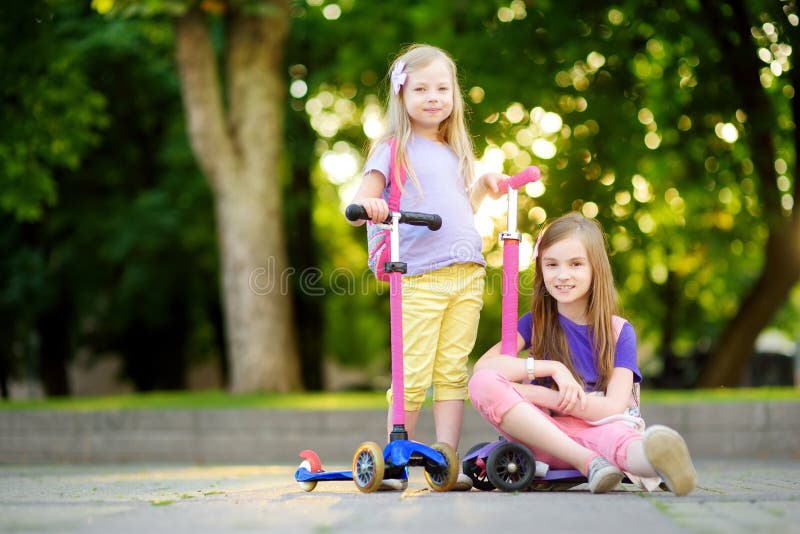 Small children learning to ride scooters in a city park on sunny summer evening. Cute little girls riding rollers. stock images Small children learning to ride scooters in a city park on sunny summer evening. Cute little girls riding rollers. stock images