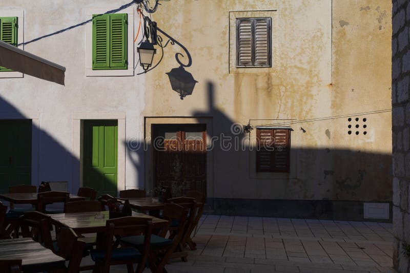 Small city square with wall lantern and empty restaurant tables in the evening long blue shadows in ancient Pag village in Croatia royalty free stock photos