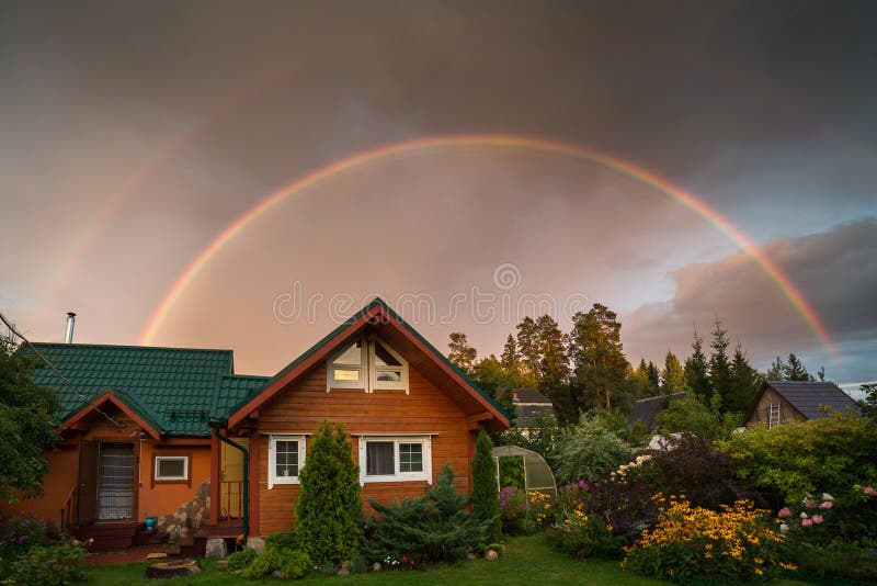 Small country house on a summer evening. Rainbow over the house. Beautiful sunset. Flowers in the garden. Russia