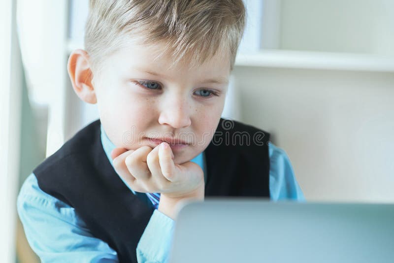 Small cute boy in business suit works at computer at office and smiling. Small business man, little boss.