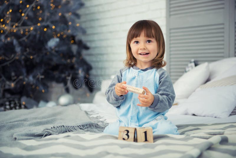 Small cute little girl is 2 years old sitting near Christmas tree and looking at the calendar. 31th of December.