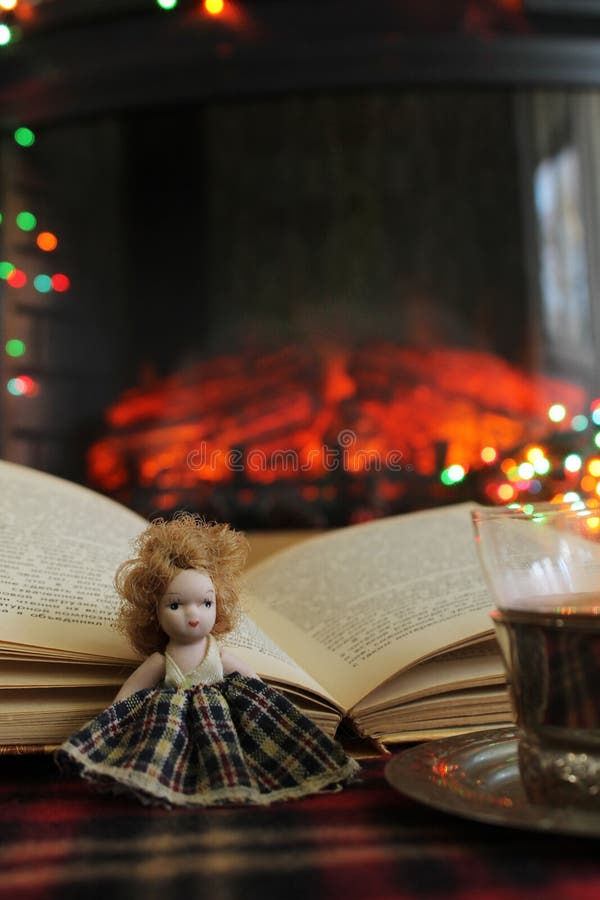 A small doll, an open book and a Cup of Cai on the background of a burning fireplace and Christmas lights, garlands royalty free stock images A small doll, an open book and a Cup of Cai on the background of a burning fireplace and Christmas lights, garlands royalty free stock images