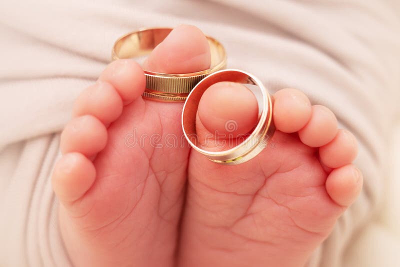 Small feets and fingers of the newborn baby with wedding rings close-up.