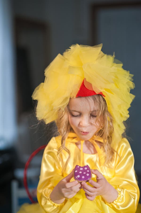 A small girl at Easter eats ginger cookies, painted eggs, laughs. Girl in the kitchen in a chicken suit royalty free stock photo A small girl at Easter eats ginger cookies, painted eggs, laughs. Girl in the kitchen in a chicken suit royalty free stock photo