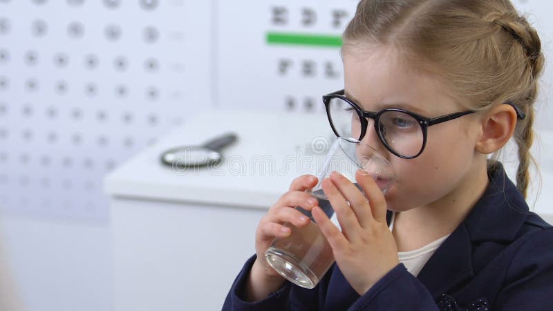 Small girl in eyeglasses taking pill with water at medical exam, treatment