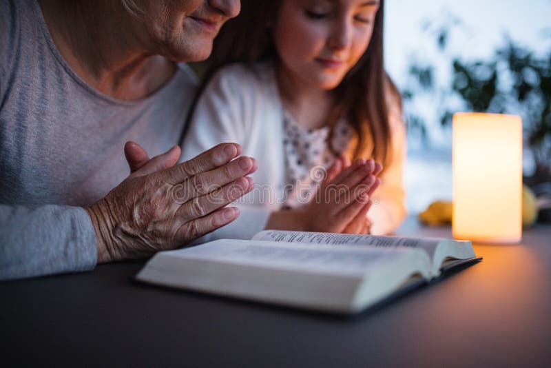 A small girl and grandmother praying at home.