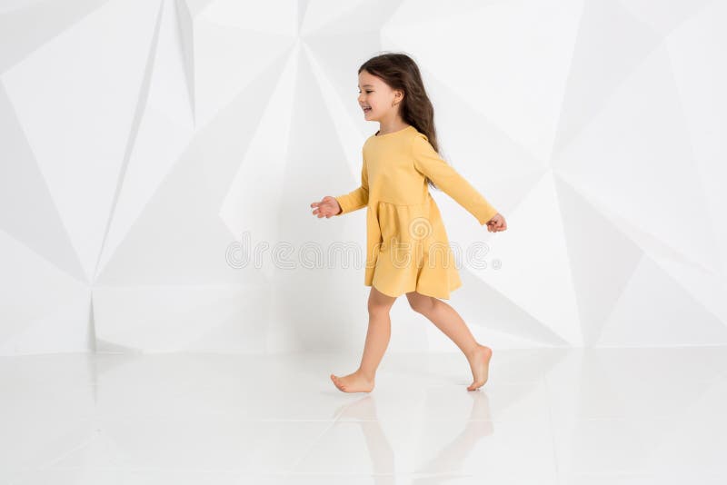Small girl wearing yellow dress dancing in studio against white background. stock photo Small girl wearing yellow dress dancing in studio against white background. stock photo