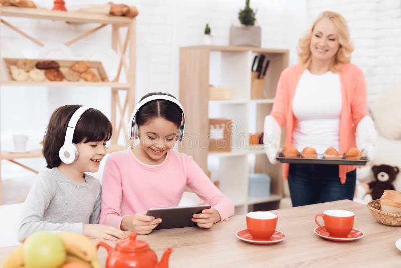 Small grandsons in headphones look at tablet in kitchen of my grandmother, who cooked cupcakes. stock image Small grandsons in headphones look at tablet in kitchen of my grandmother, who cooked cupcakes. stock image