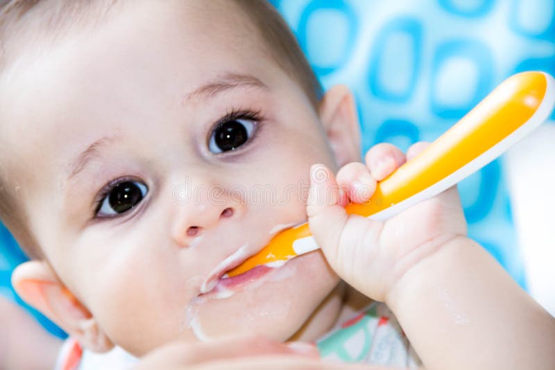 Small happy child sitting in a chair and eats yogurt from whose face is marred in baby food