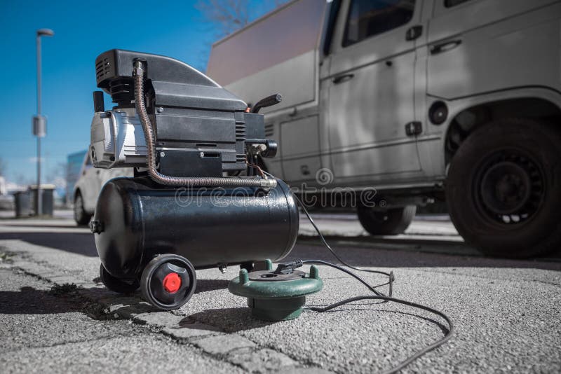 Small hobby air compressor used to pump tires or other inflatable dings, resting on a sidewalk of a town road. ready to pump an SUV tire