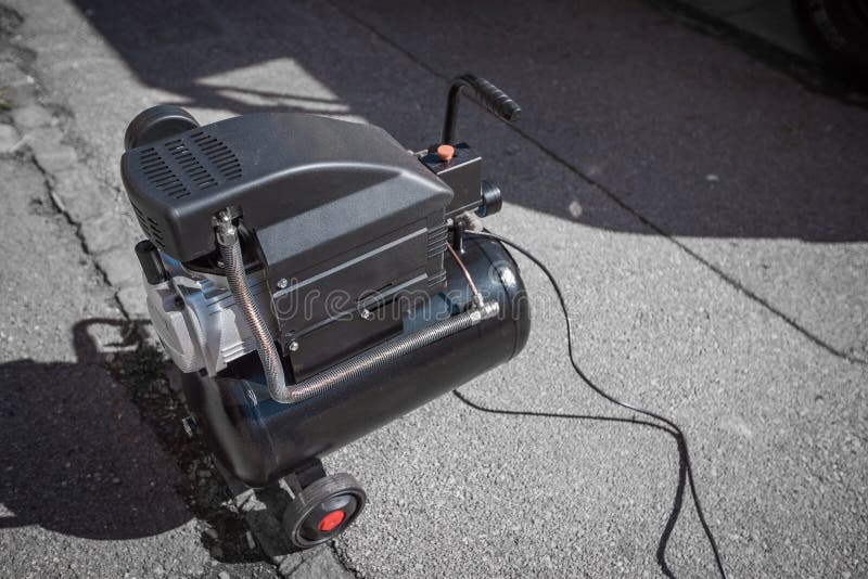 Small hobby air compressor used to pump tires or other inflatable dings, resting on a sidewalk of a town road