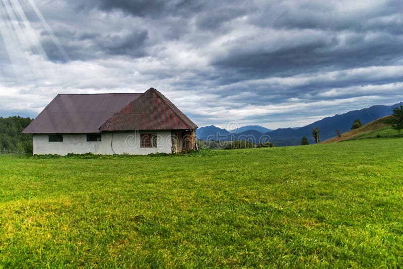 A small house, kennel, farm deposit somewhere on a yellow-green field near the mountains. An autumn day at the mountain. A dramati