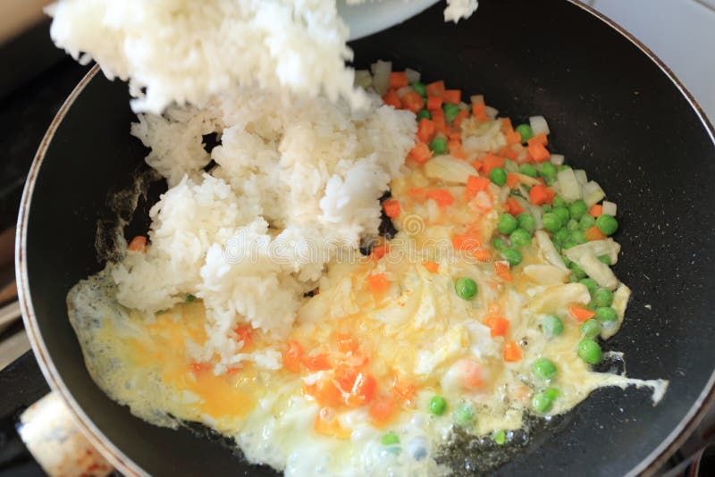 Small pieces of white onion, garlic, carrot, green peas and egg in hot iron pan in process of fried rice cooking. Asian food royalty free stock photos