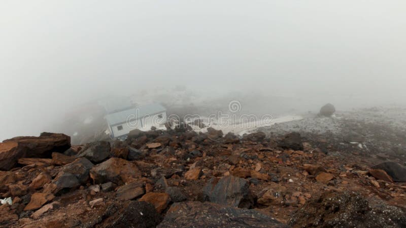 Small shelter for climbers located in mountains on a foggy and cloudy day, timelapse effect. Clip. Refuge for alpinist, small houses on a rocky slope