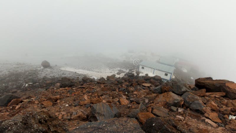 Small shelter for climbers located in mountains on a foggy and cloudy day, timelapse effect. Clip. Refuge for alpinist, small houses on a rocky slope